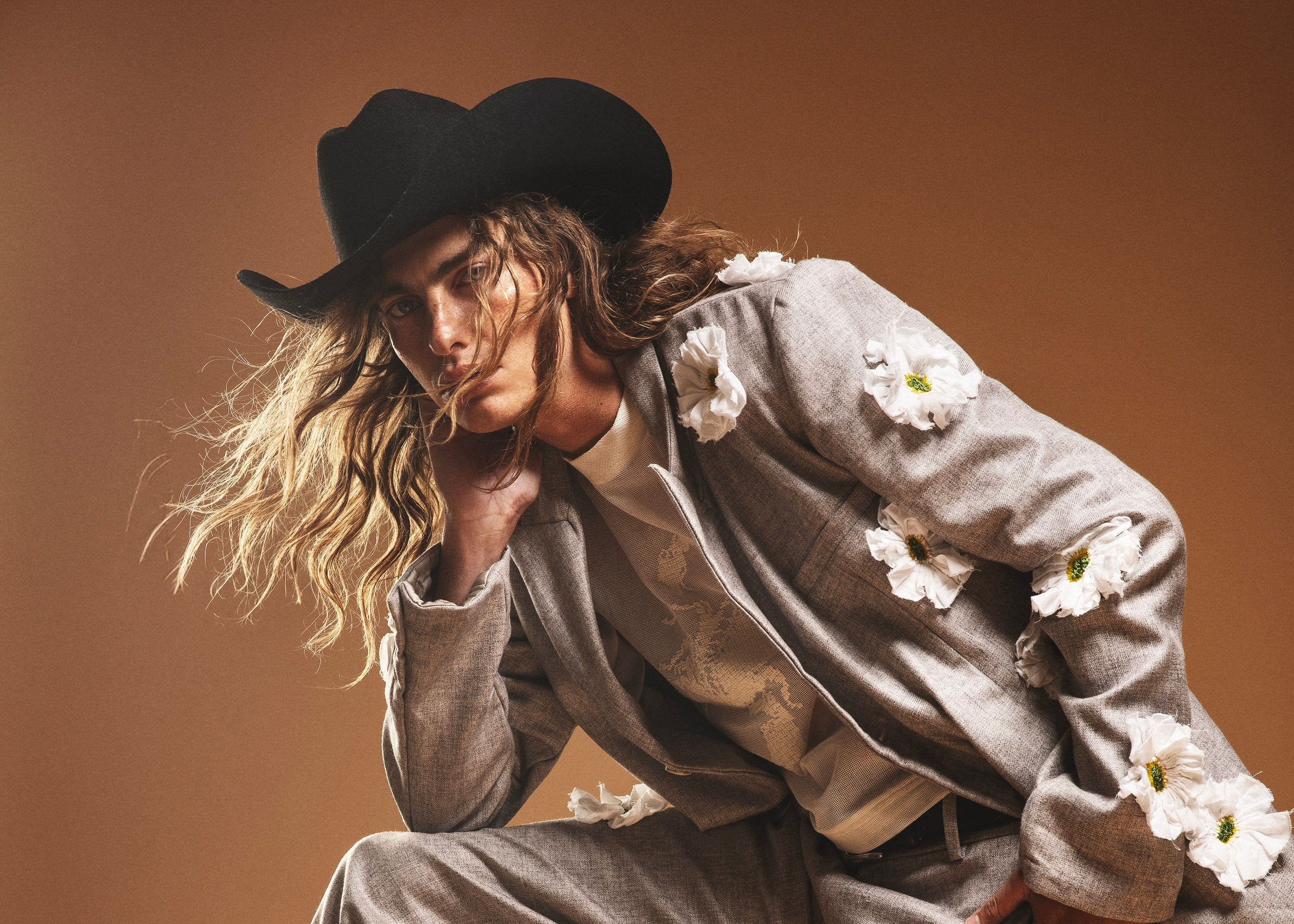 Person in a gray outfit with floral elements on a brown background