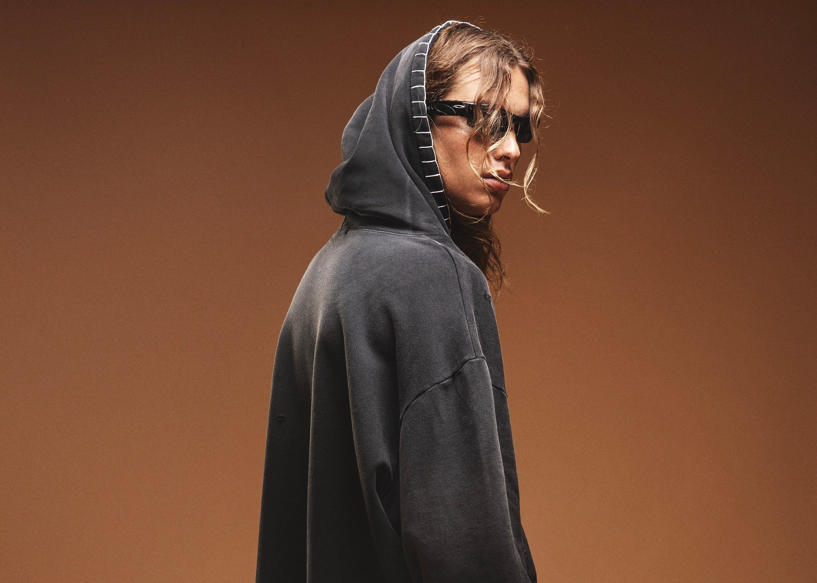 Person wearing a dark hoodie and light pink shorts against a brown background