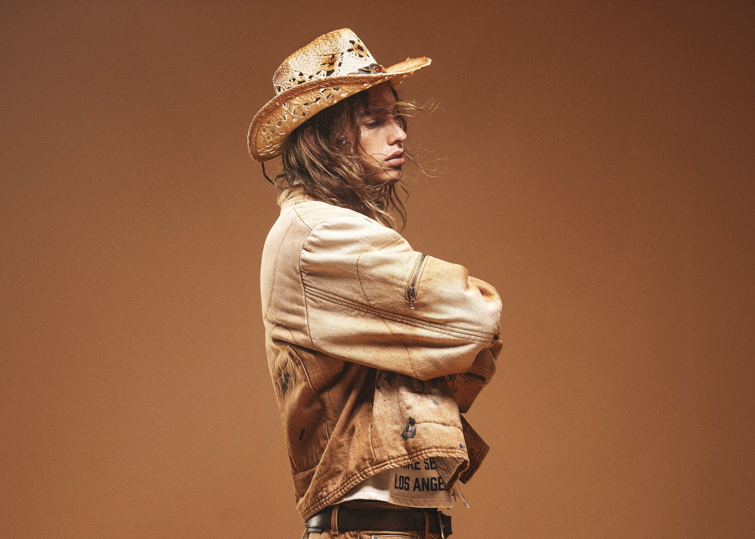 Person wearing a cowboy hat and rugged clothing against a brown background
