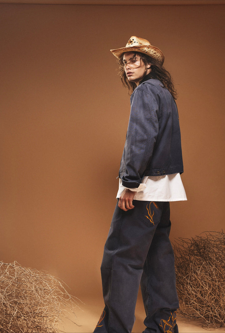 Person wearing a denim jacket and cowboy hat against a brown backdrop